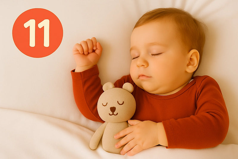 Baby mit rotem Shirt schläft mit Teddy im Arm und links steht eine 11