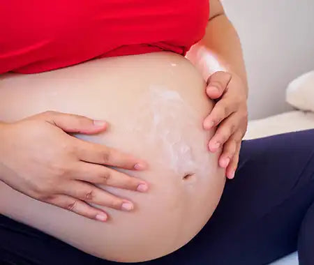 Schwangere Frau mit Creme auf dem Bauch